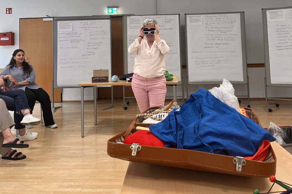 Frau mit dunkler Brille steht vor einem geöffneten Koffer